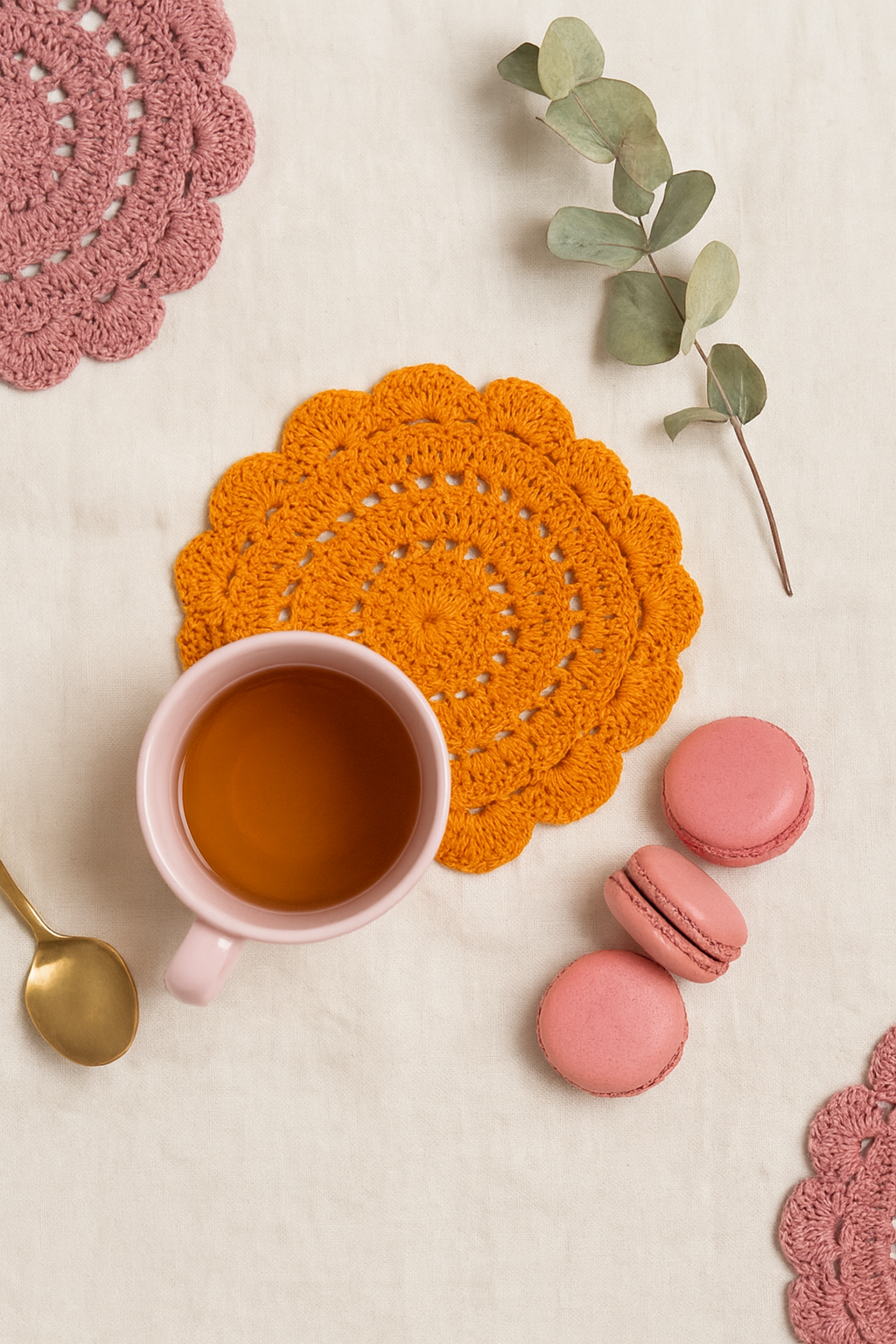 Cup of tea with pink macarons and a yellow crochet coaster on a light surface.