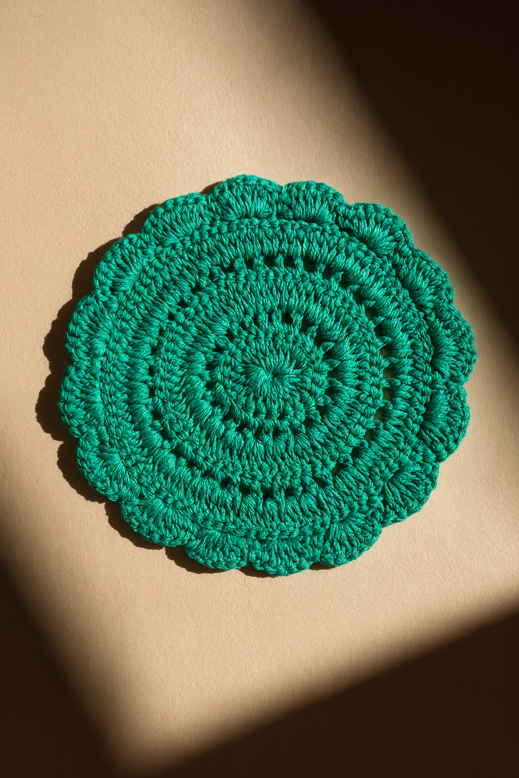 Green crocheted coaster on a beige surface