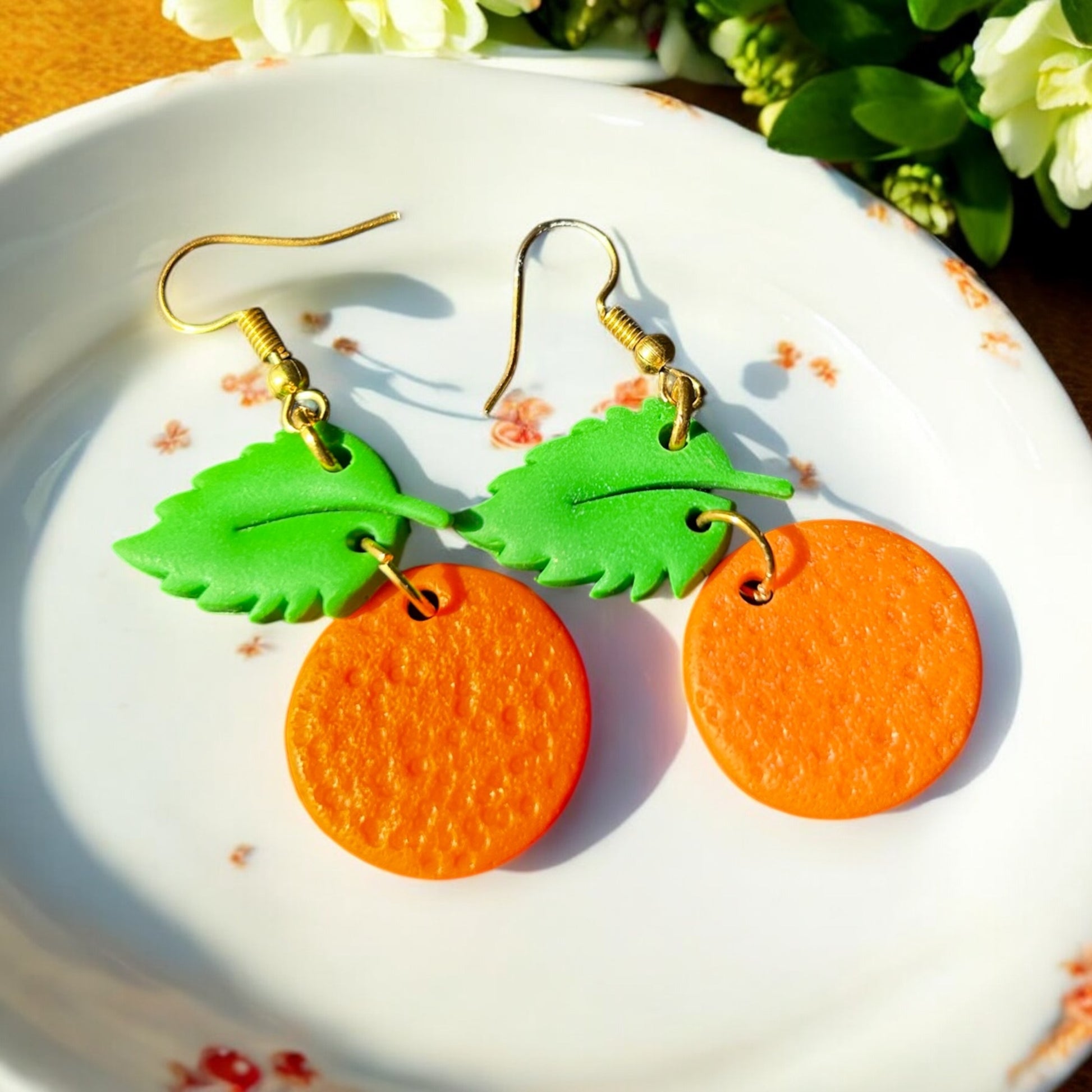 Close-up of handmade orange dangle earrings with green leaf tops