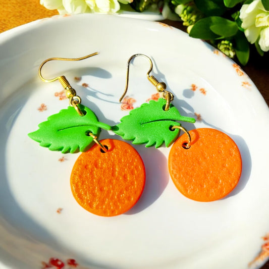 Close-up of handmade orange dangle earrings with green leaf tops