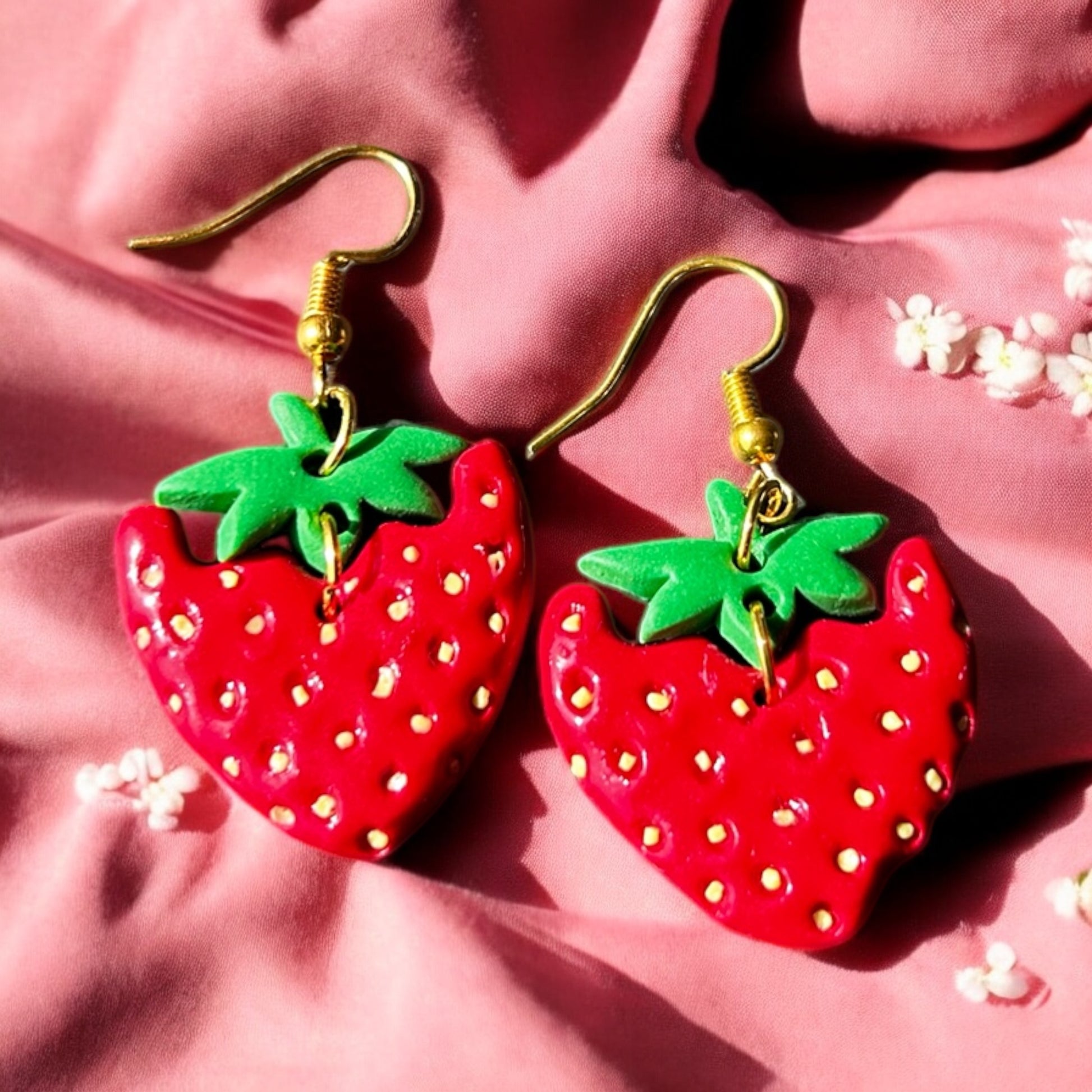 Close-up of handmade strawberry dangle earrings with green leaf tops