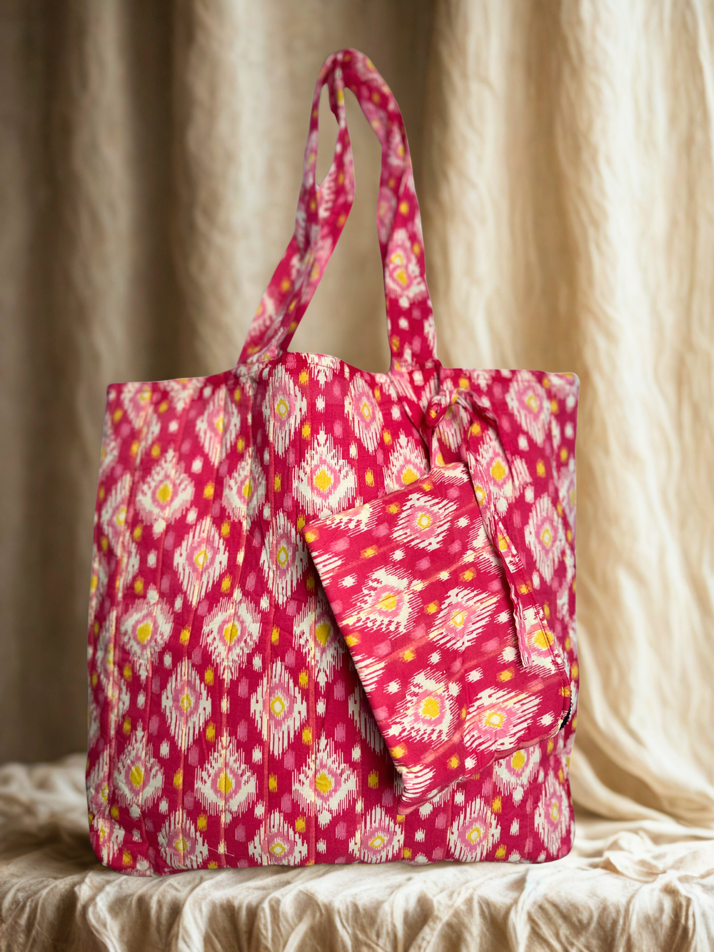 A pink patterned tote bag with matching pouch on an earthy linen background