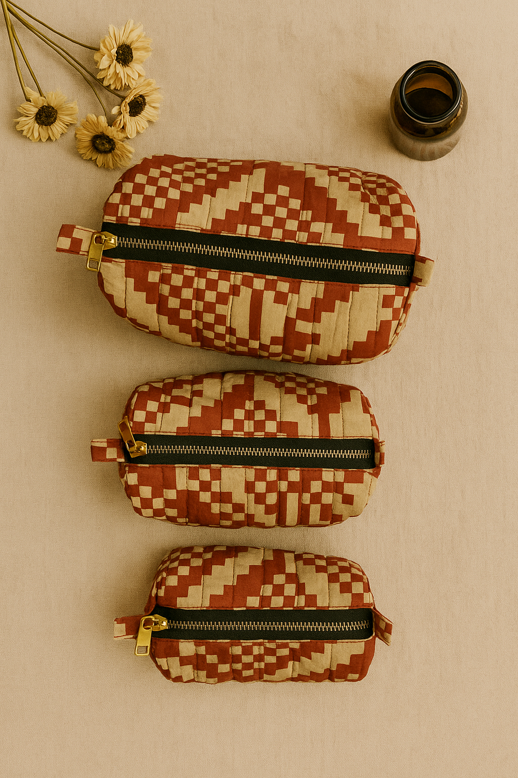 one large, one medium and one small wahser bag with geometric pattern on a plain background, some flowers on the side and a small brown glass bottle. 