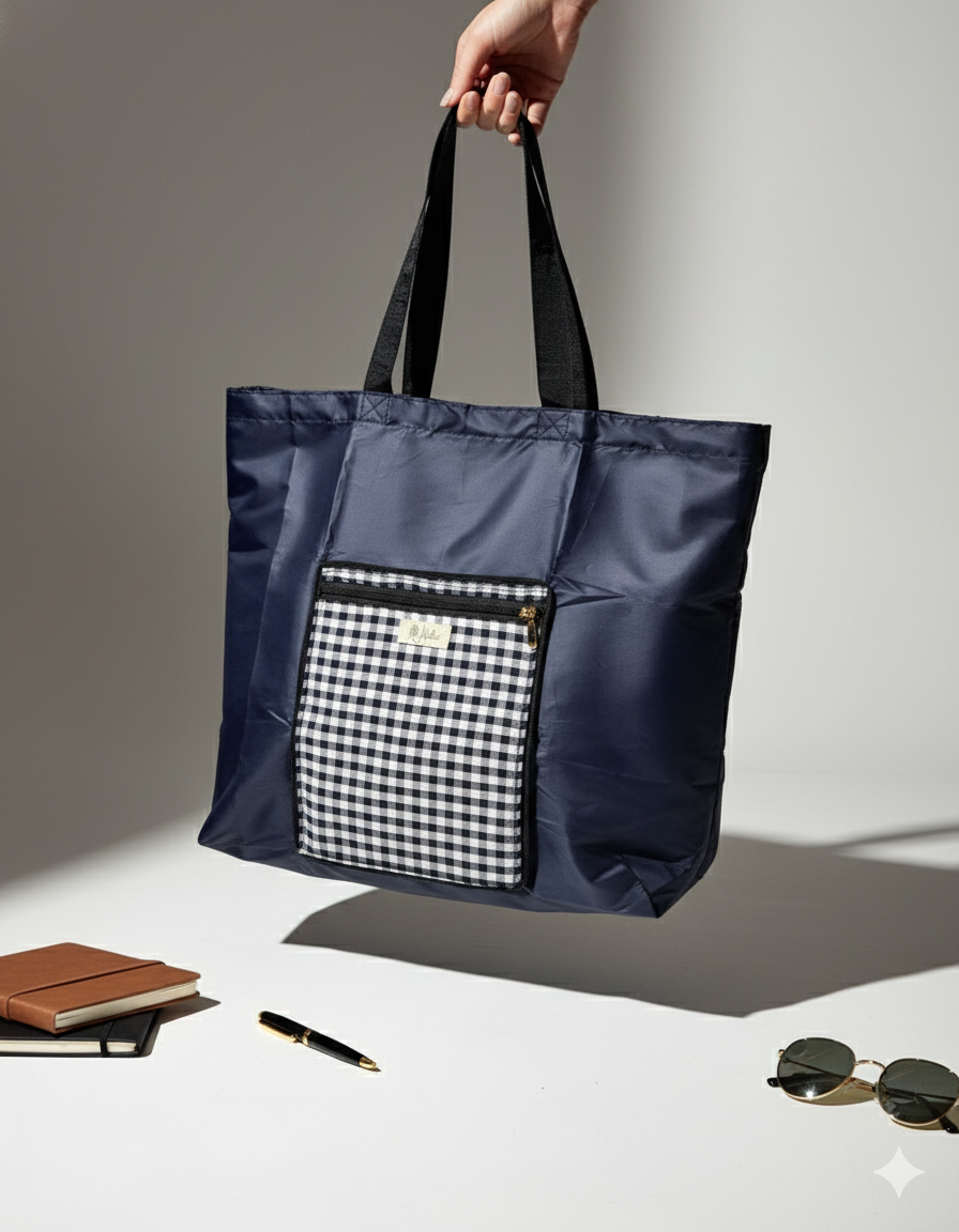 Navy blue tote bag with a gingham patterned pocket held by a hand on a light background.
