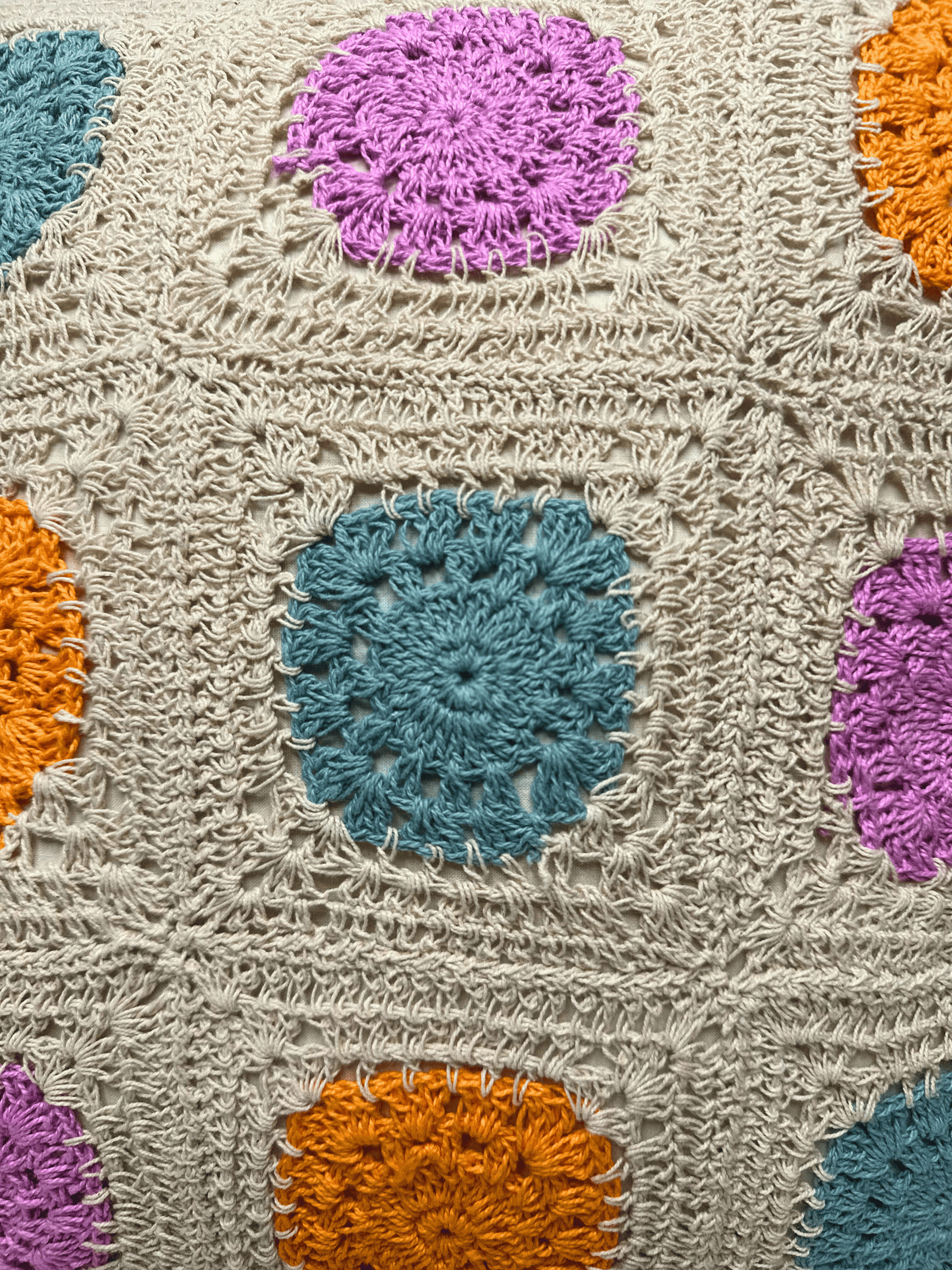 Crocheted cushion cover with colorful circular patterns on a beige background