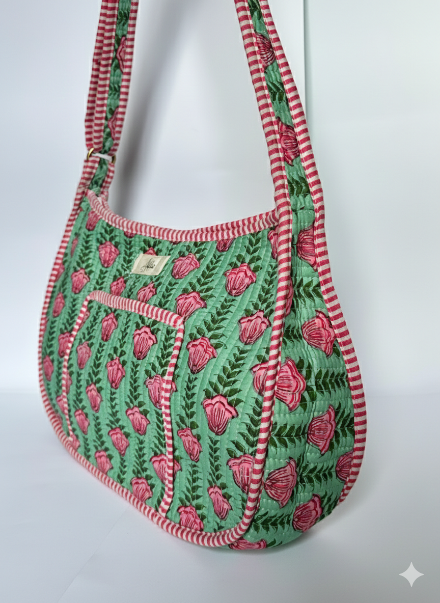 Green and pink floral pattern quilted crossbody bag with adjustable straps, front pocket, thick sides and red striped handle on a white background