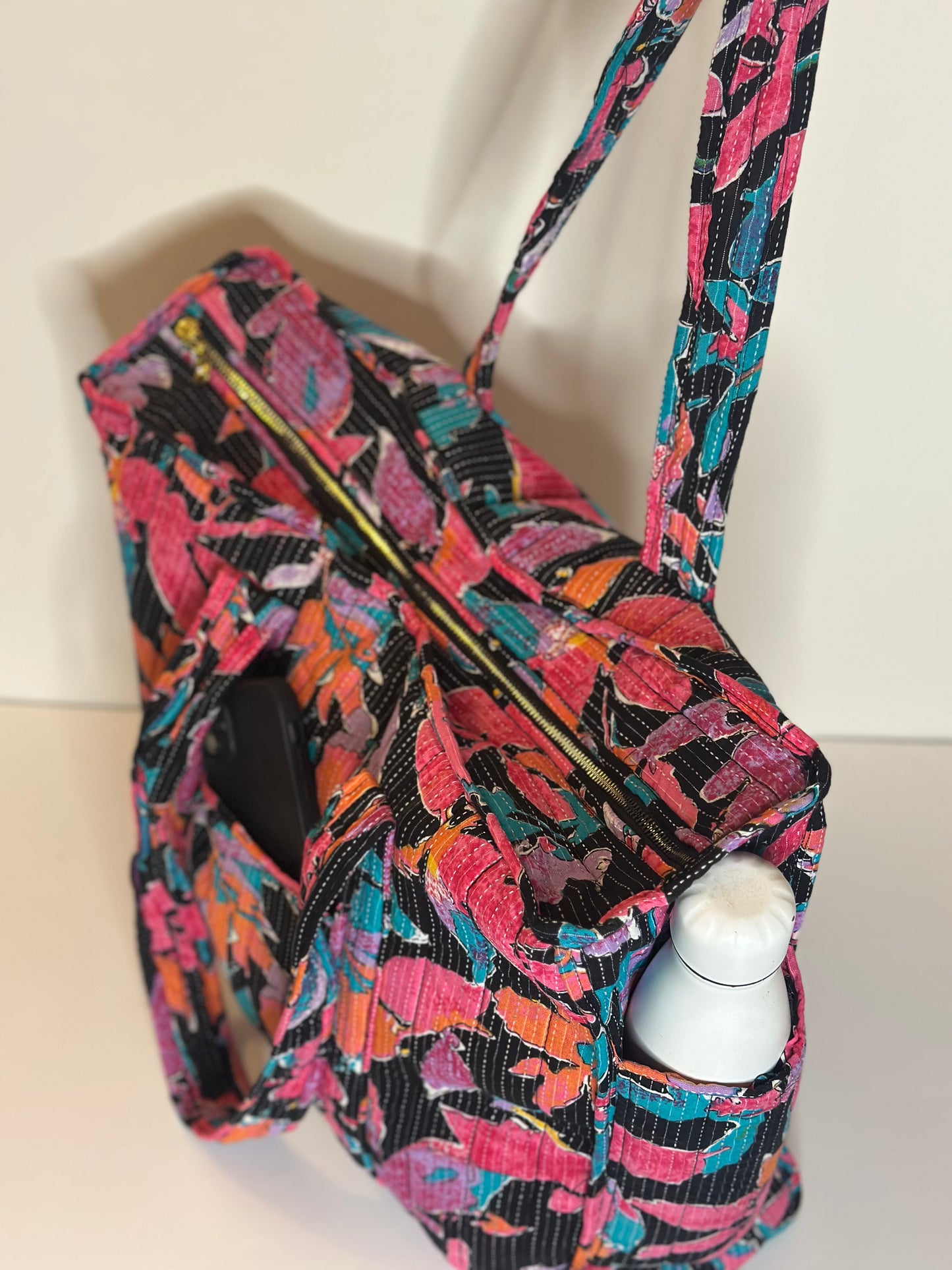A colourful floral patterned bag with a bottle in the side pocket inside on a white background