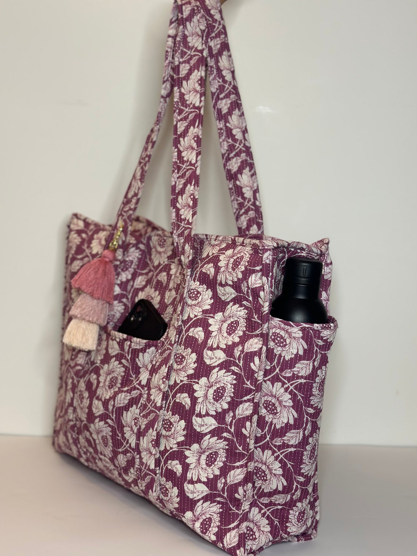 Floral-patterned tote bag with a black bottle inside on a white background