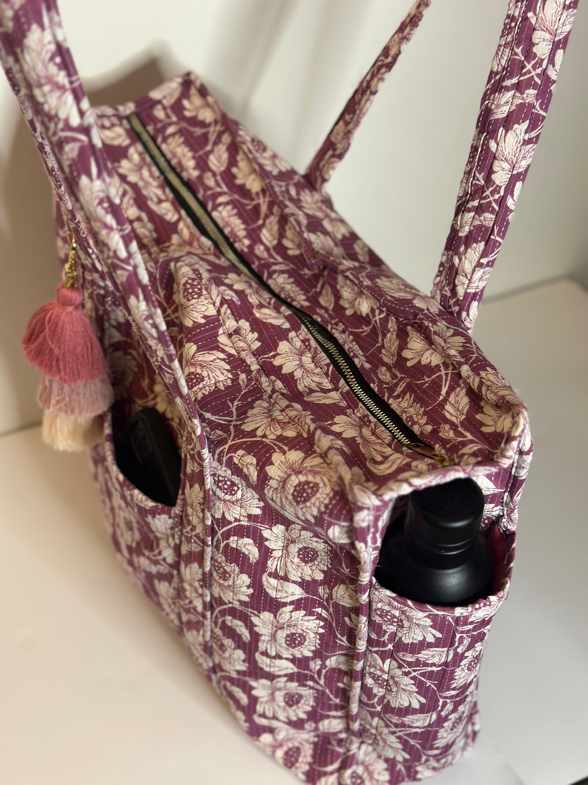 Floral-patterned tote bag  with zipper with black bottles inside on a white background