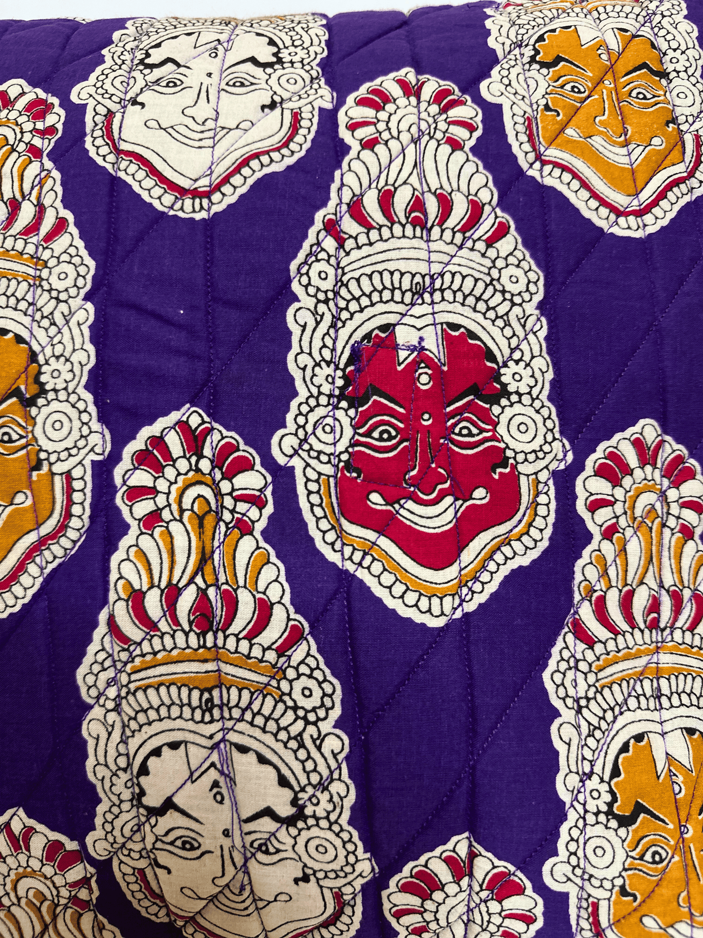 Decorative quilted cushion fabric with colourful face mask patterns on a purple background